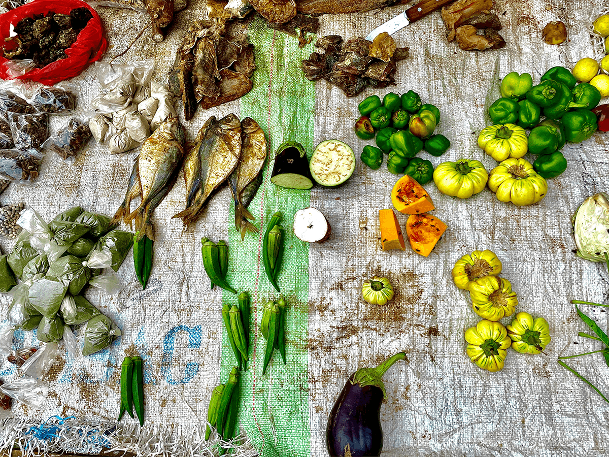 Various produce and fish are grouped toegether and laid out on a blanket